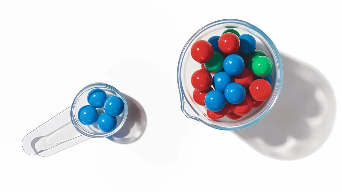 Large transparent container filled with multicolored marbles with a small scoop containing only a few marbles showing a completely uniform color distribution. Demonstrates how small sample sizes can misrepresent the true population.